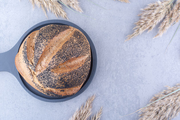 面包把涂有黑芝麻的面包条放在一个平底锅里 旁边是大理石表面的干羽毛草茎外壳种子面包