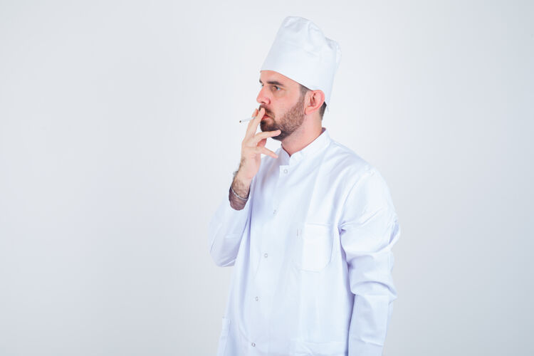 食材年轻男厨师的画像 穿着白色制服抽烟 正看着若有所思的前视图厨师男人思想美味