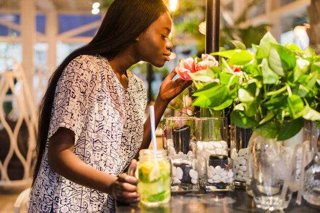 年轻在咖啡馆里 一位身着夏装的非洲裔美国年轻女子 兴高采烈地嗅着花瓶里的白花人水仙咖啡馆
