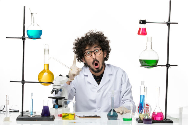 科学前视图穿着医疗服的男性化学家正坐在桌子前面 空白处有溶液化学医学坐着
