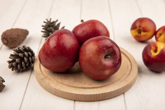 特写俯瞰美味的红苹果在一个木制的厨房板与桃子和松果隔离在一个白色的木制表面美味饮食食品