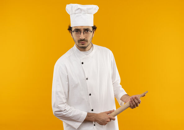 黄色自信的年轻男厨师穿着厨师制服 戴着眼镜拿着擀面杖穿烹饪男性