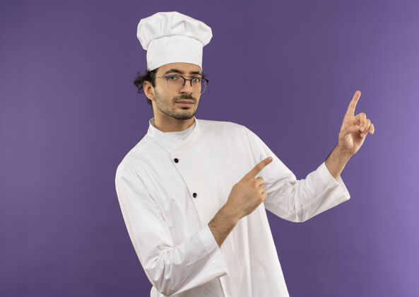 男年轻的男厨师穿着厨师制服 戴着眼镜指着旁边壁板烹饪紫色