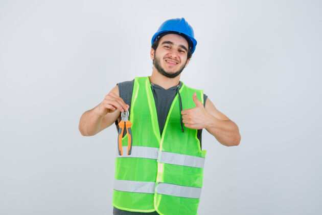 人年轻的建筑工人拿着钳子 大拇指朝上 穿着工作服 看上去很高兴前视图肖像前面圣诞节