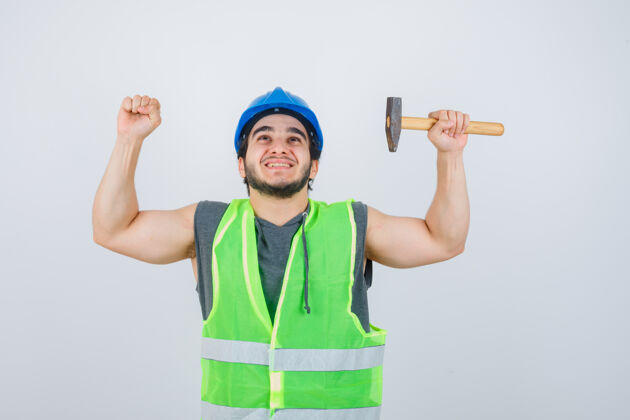积极年轻的建筑工人拿着锤子 穿着工装展示获奖者的姿态 看上去很幸运正视图时尚而搞笑