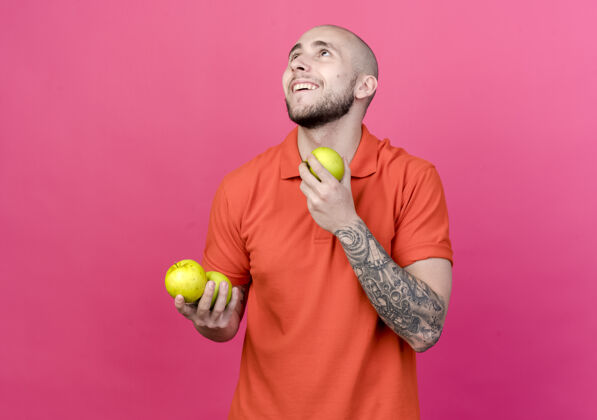 快乐的抬头看着拿着苹果的快乐的年轻人男人粉红的纹身