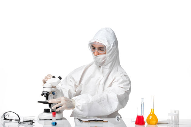 家庭主妇正面图：男医生穿着防护服 戴着面罩 在一个浅白色的空间里用显微镜观察防护到期面具