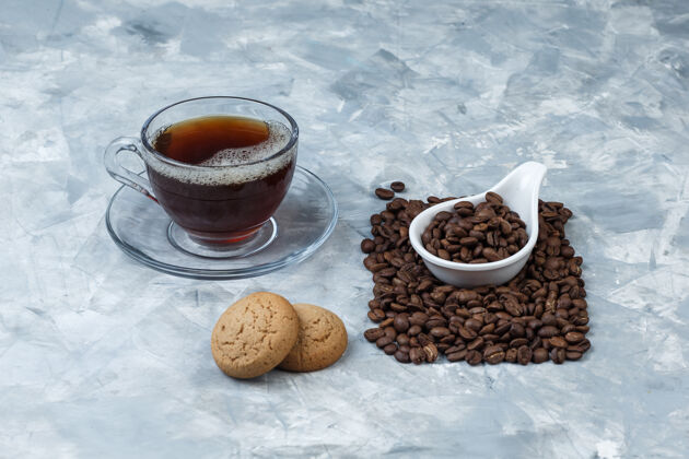 卡布奇诺一些咖啡豆配曲奇饼 一杯咖啡放在蓝色大理石背景的白色瓷壶里 特写镜头粗麻布芳香食物