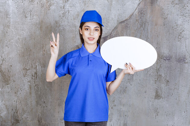 销售身着蓝色制服的女服务人员手持椭圆形信息板 并显示积极的手势休闲操作员活动