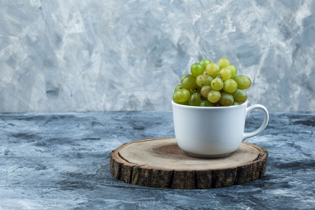 果汁侧视图绿色葡萄在白色的杯子上 在粗糙的石膏和木片背景上水平营养季节夏天