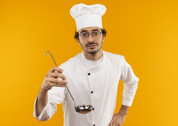 手年轻的男厨师穿着厨师制服 戴着眼镜 手举勺子放在臀部手持男人臀部