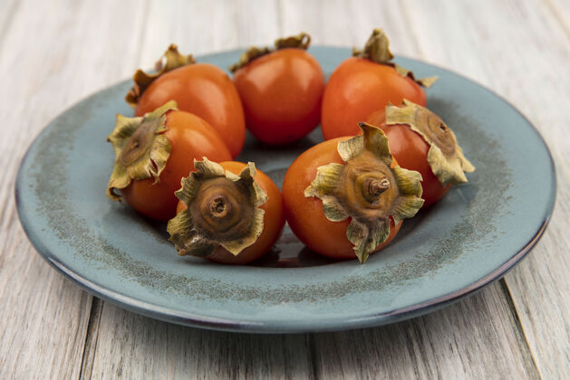 甜点在灰色木质表面的盘子上 可以看到柔软的新鲜柿子的顶视图健康秋季柔软
