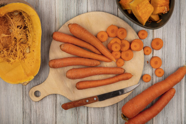 胡萝卜顶视图橙色根蔬菜胡萝卜在一个木制的厨房板与切碎的胡萝卜用刀与半南瓜在一个灰色的木制表面一半沙拉厨房