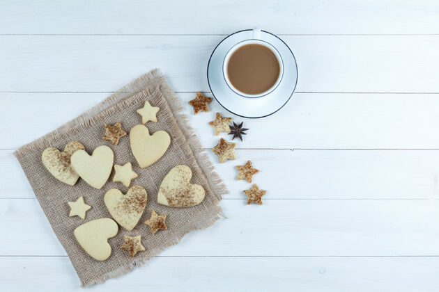 架子心形和星型饼干放在一个装有星型饼干的袋子上 一杯咖啡平放在一块白色的木板背景上糕点蛋糕奶油