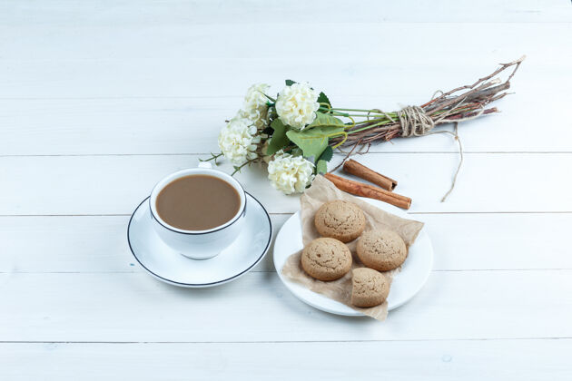 餐桌饼干放在一个白色的盘子里 咖啡 肉桂 鲜花放在白色的木板背景上高角度观看结块生日咖啡