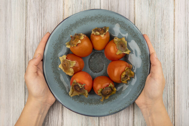 盘子女性手拿着一盘甜甜的新鲜柿子放在灰色木头表面的俯视图饮食木头健康