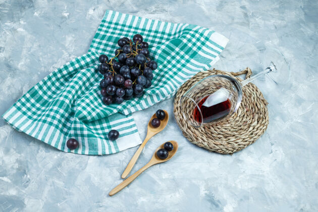 石膏把黑葡萄平铺在木勺里 放上一杯葡萄酒 放在石膏上的垫子和厨房毛巾的背景上水平木材水平甜点