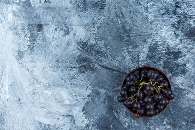 石膏黑葡萄在一个粘土碗平躺在一个肮脏的石膏背景素食葡萄藤小