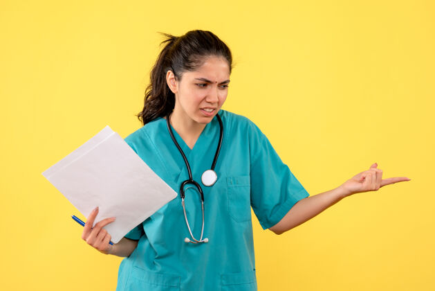 制服前视图愤怒的女医生穿着制服拿着黄色背景的文件女医生愤怒健康