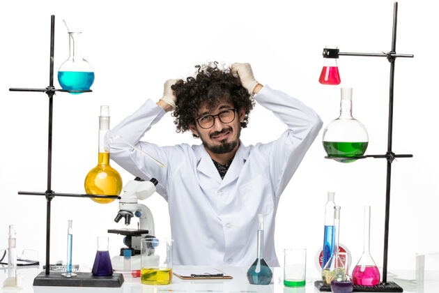 头发前视图穿着医疗服的男性化学家坐在桌子前 用溶液在白色空间撕扯他的头发溶液医学正义