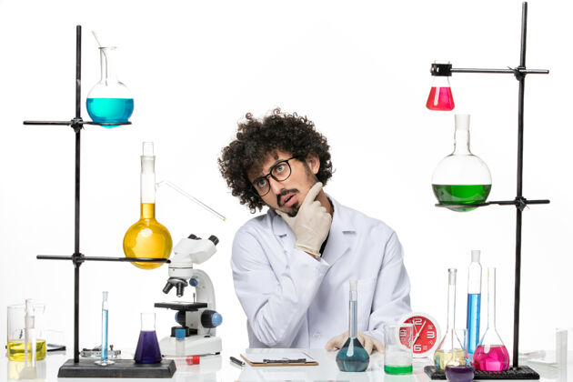 男化学家正面图身着医疗服的男性化学家正坐在桌子前 思考着白色空间的解决方案科学实验室化学