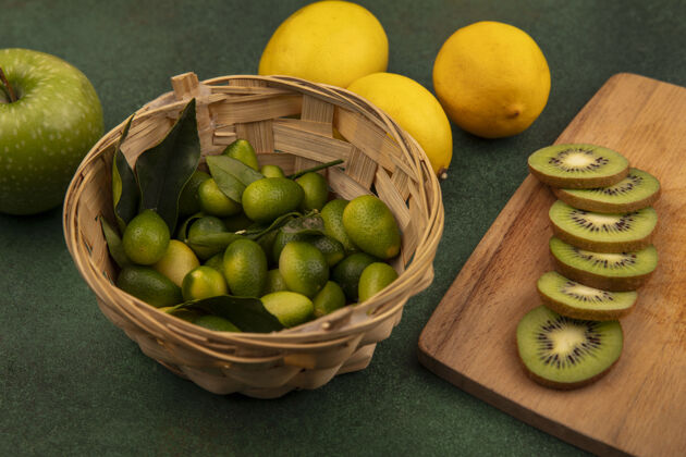 营养木制厨房板上美味的猕猴桃切片俯视图 桶上放着金盏花 绿色表面上隔离着柠檬和苹果苹果热带厨房