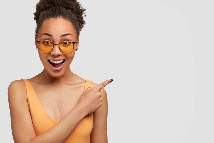 美国人积极的黑人女孩有卷发 用食指指着旁边Joy女性Hipster