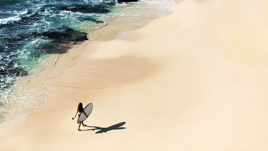 日落美丽的女孩拿着冲浪板走在荒野的海滩上从山顶看风景很美海洋海洋年轻
