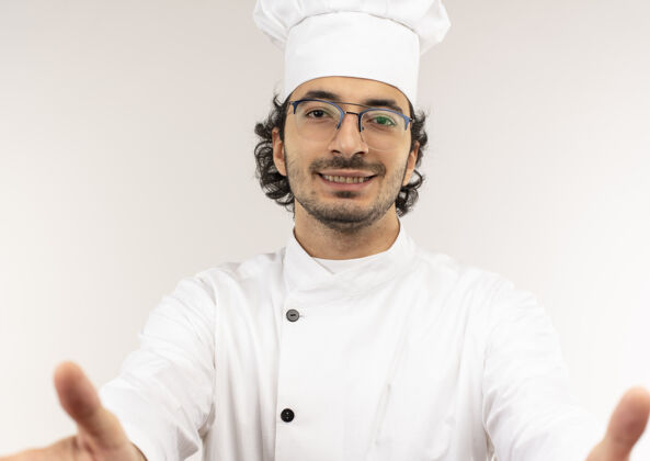 制服面带微笑的年轻男厨师穿着厨师制服 戴着眼镜 隔离在白色的墙上烹饪厨师年轻
