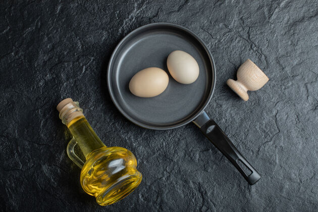 配料黑色的煎锅里有一个生鸡蛋和一瓶隔离在白色背景上的油处理早餐健康