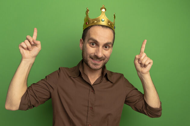 年轻戴着王冠的年轻高加索男子微笑着 孤零零地站在绿色的墙上戴上微笑男人