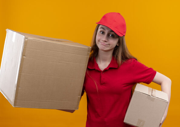 盒子穿着红色制服的年轻女送货员把箱子放在孤立的橙色墙上女人年轻分娩