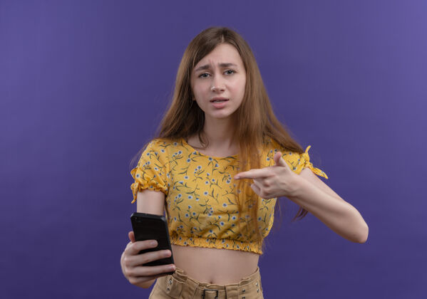 电话年轻女孩拿着手机 指着隔离的紫色墙壁上的手机 留着复印空间女孩拿着指着