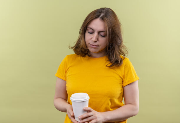 放下年轻随意的女人拿着塑料咖啡杯 在有复印空间的绿色隔离墙上俯视着它休闲塑料拿着