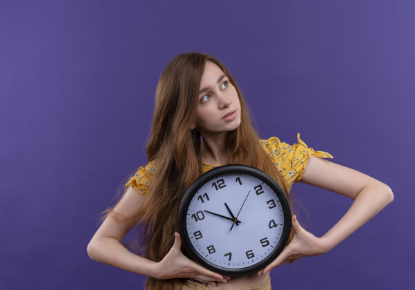 抱着一个体贴的年轻女孩拿着钟 看着孤立的紫色墙上的右边女孩对时钟
