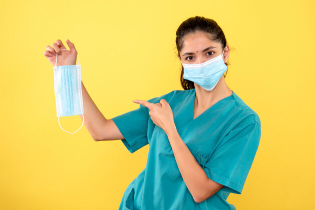 医学黄色墙壁上的年轻女性正对着手中的面罩 戴着医用面罩正面医院手