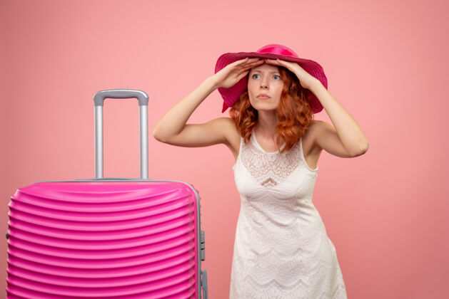 模型年轻的女性游客与粉红色的帽子和粉红色的墙壁上的包的正面视图包人可爱