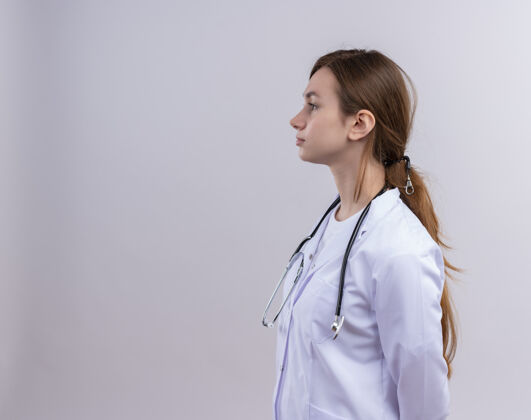 听诊器穿着医用长袍和听诊器的年轻女医生站在隔离的白色墙壁上的侧视图中 有复印空间穿着年轻人女士