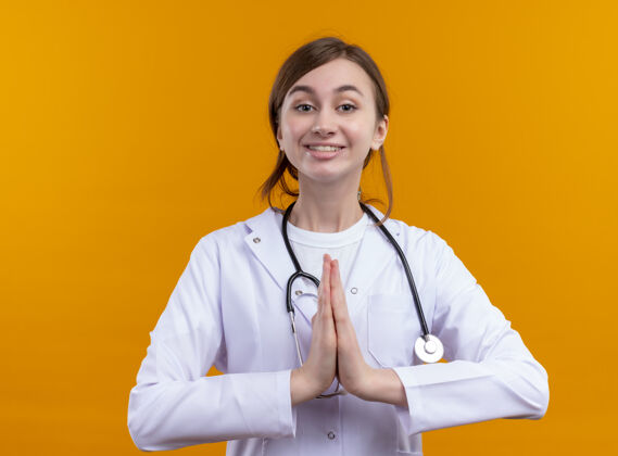 医学面带微笑的年轻女医生 穿着医用长袍 戴着听诊器 把双手放在隔离的橙色墙上长袍女人医生