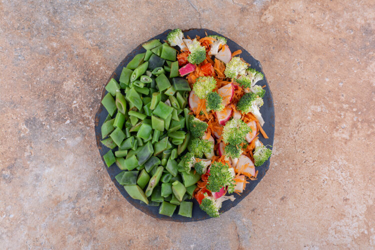 托盘一小盘混合蔬菜沙拉和切碎的豆荚放在大理石表面萝卜胡萝卜脉冲
