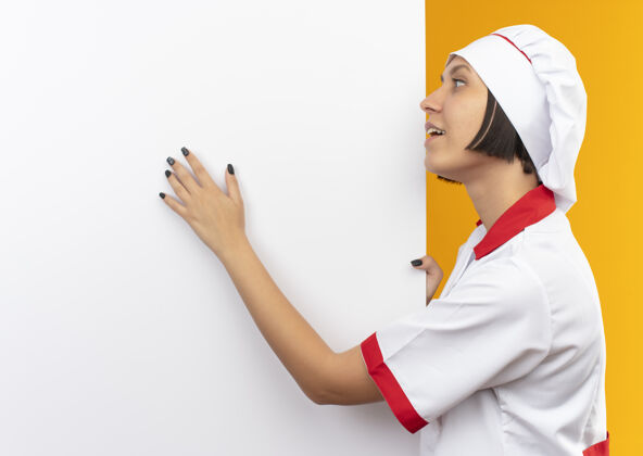 印象穿着厨师制服的年轻女厨师站在白色的墙壁旁 手挽着手 看着橙色的房间里孤立着的那只手烹饪持有空间