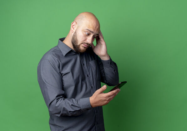手机印象深刻的年轻秃头呼叫中心男子拿着手机 看着手机和触摸头隔离在绿色与复制空间秃顶男人年轻