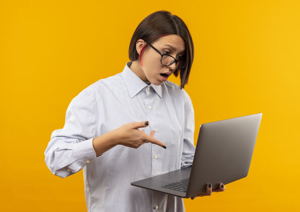 穿着印象深刻的年轻呼叫中心女孩戴着眼镜拿着看 指着笔记本电脑孤立的橙色电话印象年轻