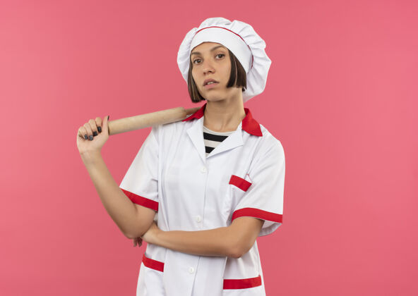 年轻自信的年轻女厨师穿着厨师制服拿着擀面杖 看起来孤立的粉红色和复制空间制服信心卷