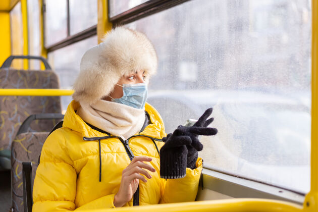 安全一幅阳光明媚的肖像画 描绘了一个冬天 穿着暖和衣服 手里拿着手机 坐在城市公共汽车上的年轻女子道路公共防护