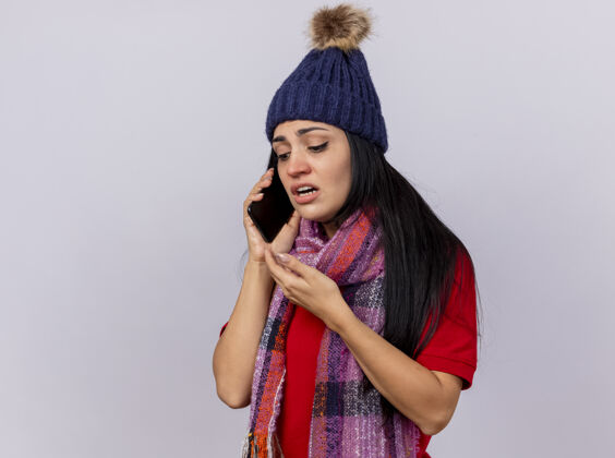 空气虚弱的年轻白种人生病的女孩戴着冬天的帽子和围巾打电话 手举在空中 在白色的背景下看着孤立的复制空间围巾帽子虚弱