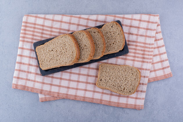 酵母在大理石表面的折叠毛巾上放一盘切片的棕色面包健康面粉烘焙食品