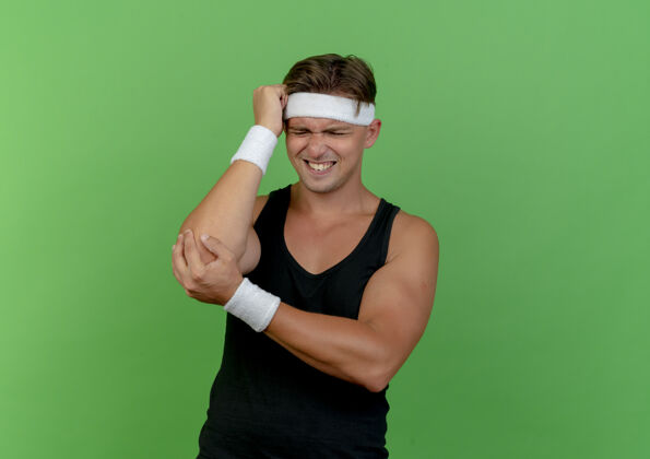 穿疼痛的年轻英俊的运动型男子戴着头带和腕带 手放在头上 另一只手放在手肘上 忍受着疼痛隔离在绿色的复制空间肘部绿色一个