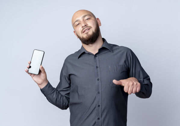 年轻自信的年轻秃头呼叫中心男子显示手机 并指着它孤立的白色秃头指向自信