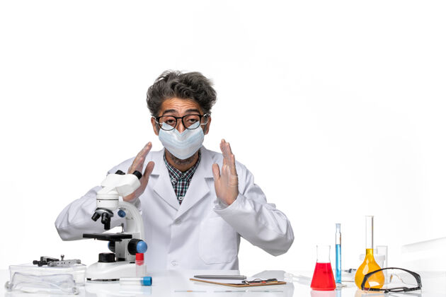 专业正面图身着特殊套装的中年科学家围坐在桌子旁 拿着解决方案化学科学医学